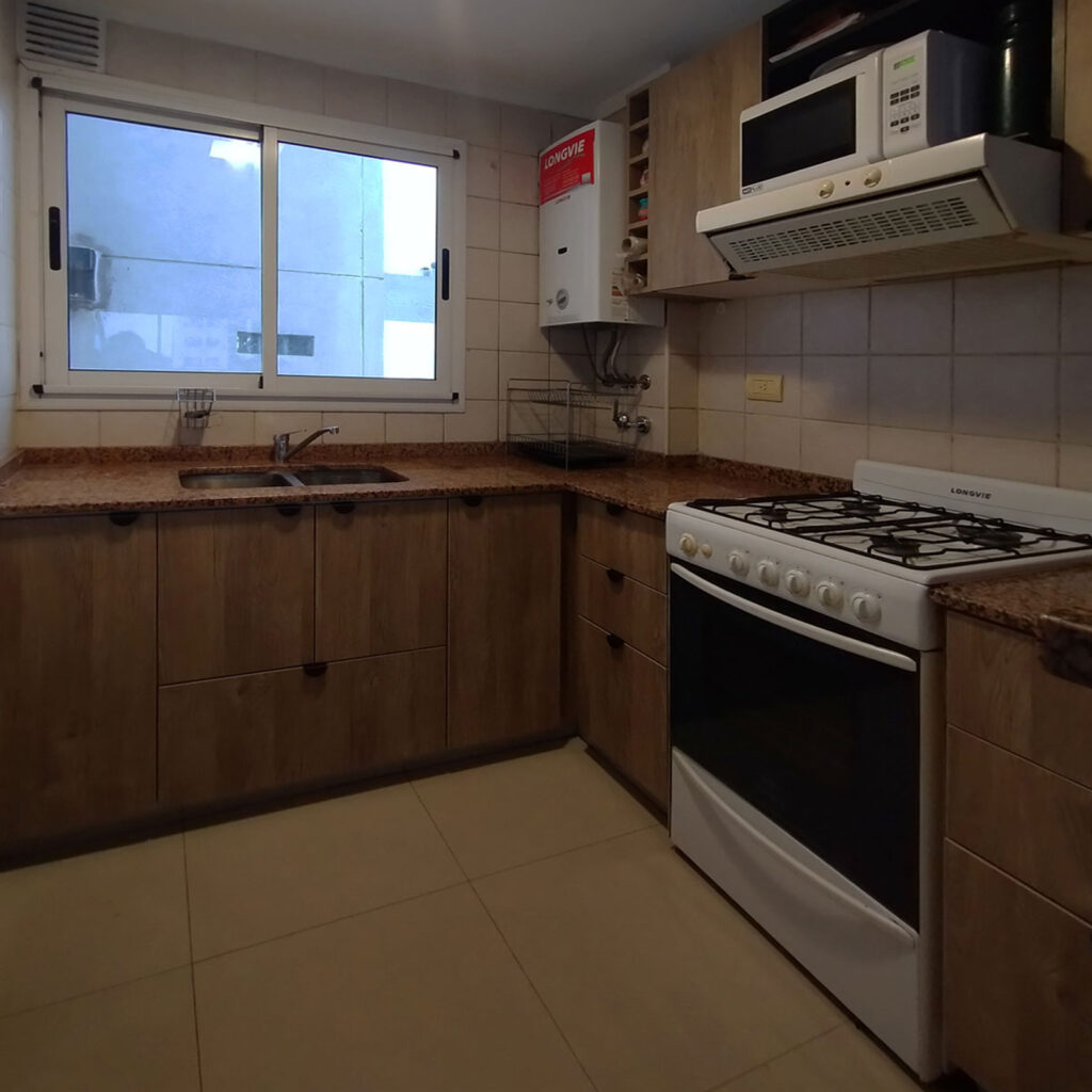 Vista general de cocina chica con módulos optimizados, bajo mesada con cajoneras y alacenas en melamina caju.