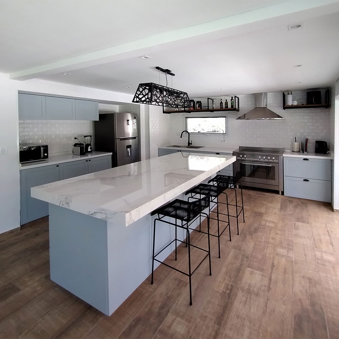 Cocina amplia con isla central y desayunador, muebles laqueados color gris y mesada en silestone símil mármol.